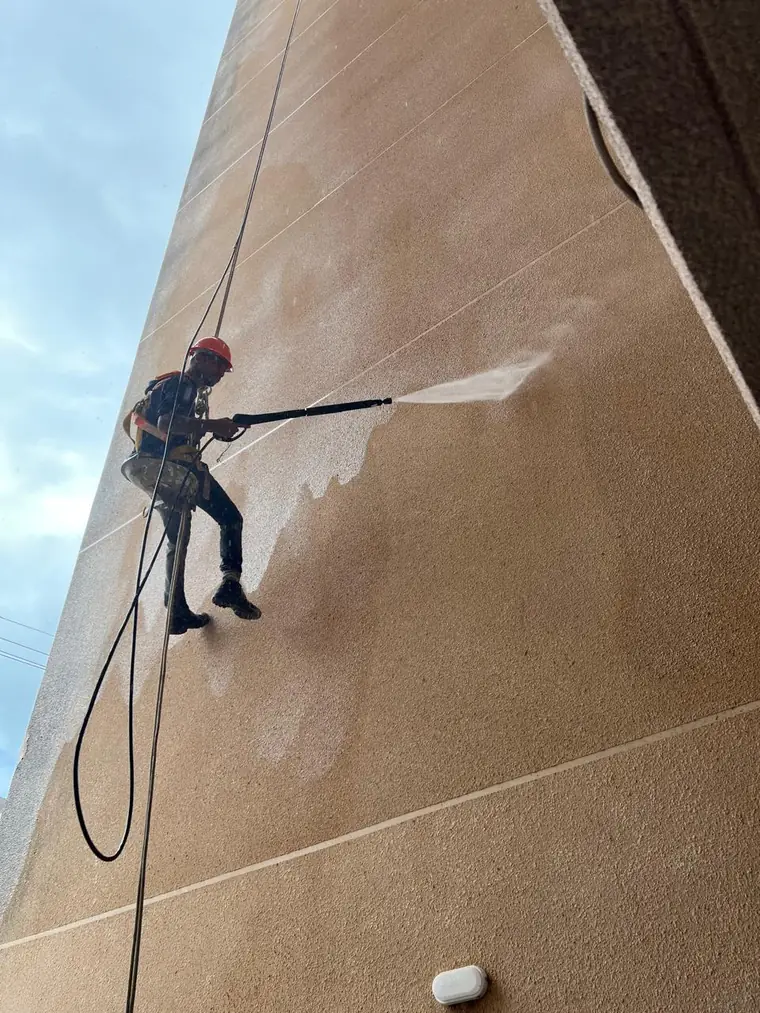 Profissional da M7 Pinturas lavando a fachada de um edifício com jato de alta pressão em acesso por corda